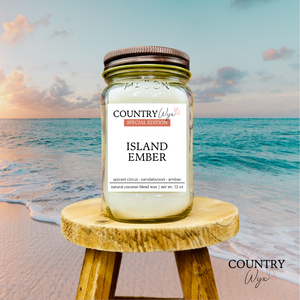Island Ember 16oz candle by Country Wyx on a wooden stool with a beach background
