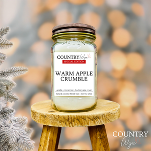 Warm Apple Crumble 16oz candle by Country Wyx on a wooden stool with a frosted pine tree holiday background