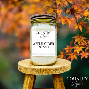 Apple Cider Donut 16oz candle by Country Wyx on a wooden stool with autumn leaves in the background