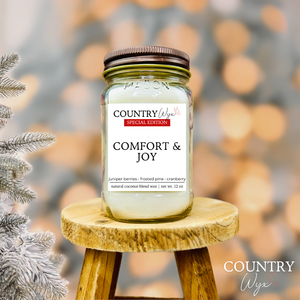 Comfort & Joy 16oz candle by Country Wyx on a wooden stool with a frosted pine tree holiday background