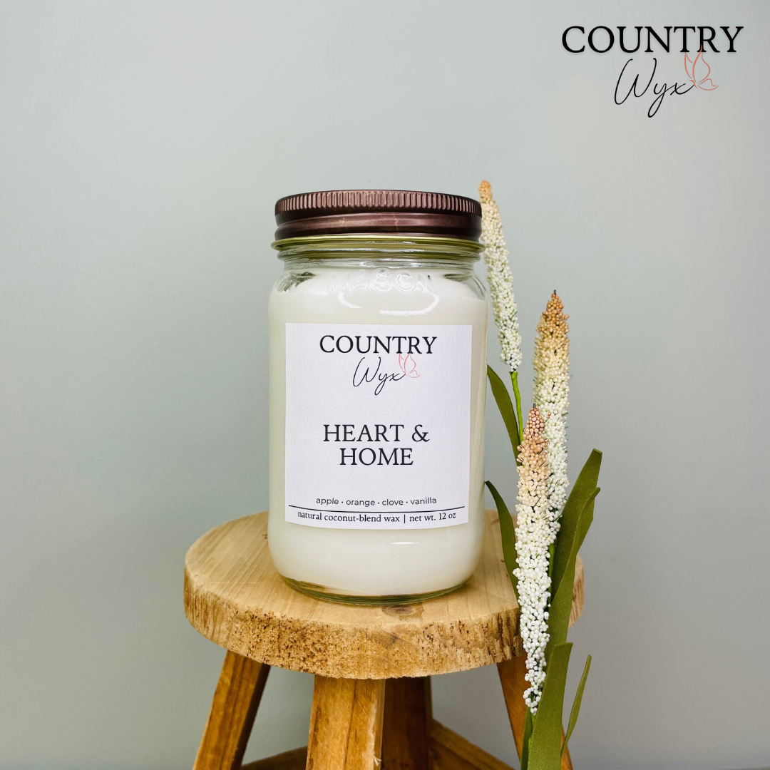 Heart &amp; Home 16oz candle by Country Wyx displayed on a wooden stool with a soft farmhouse-inspired background