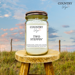 Two Steppin' 16oz candle by Country Wyx on a wooden stool with a Nebraska Sandhills background