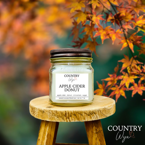 Apple Cider Donut 8oz candle by Country Wyx on a wooden stool with autumn leaves in the background