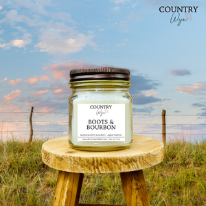 Boots & Bourbon 8oz candle by Country Wyx on a wooden stool with a Nebraska Sandhills background