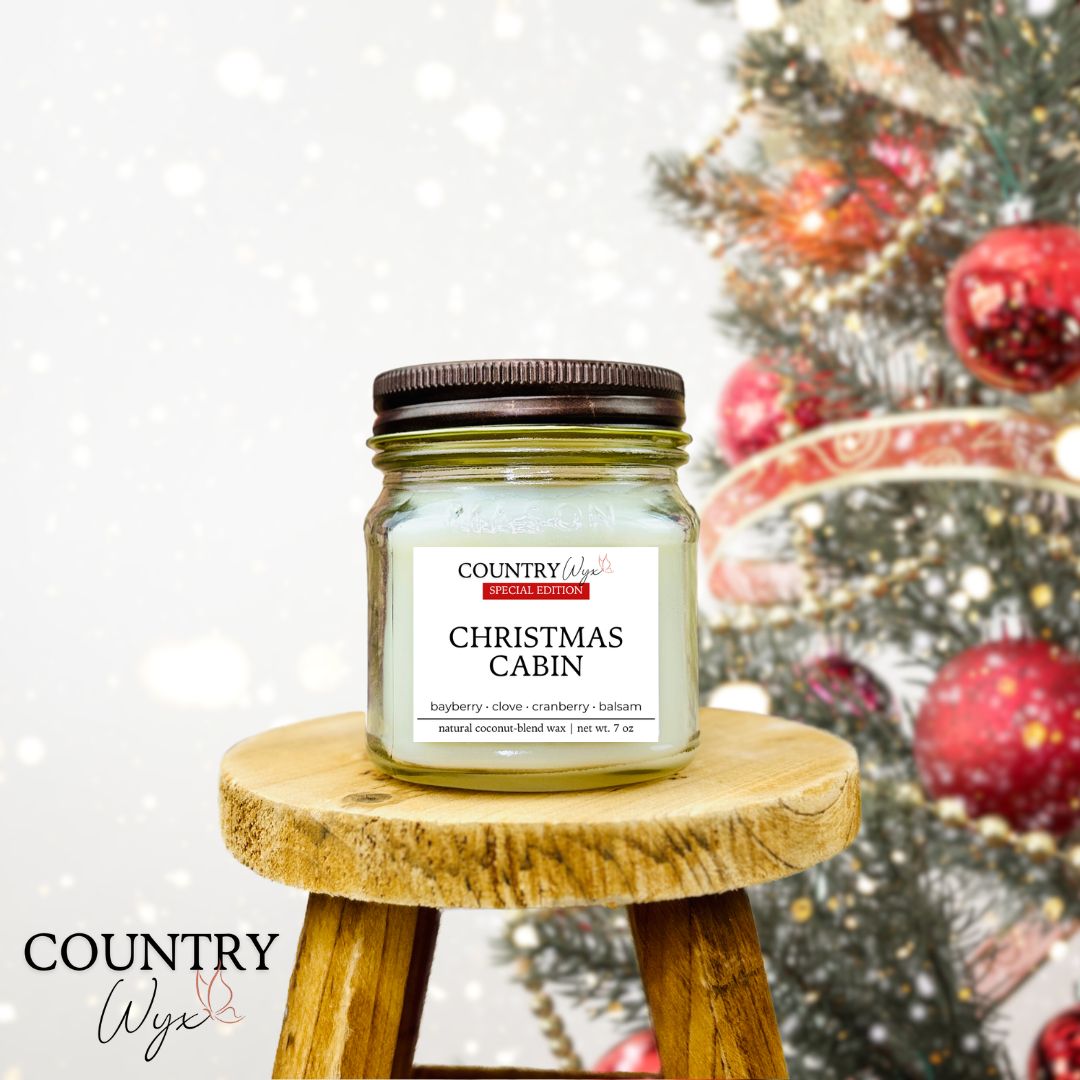 Country Wyx 8oz Christmas Cabin mason jar candle on a wooden stool with a decorated Christmas tree in the background.