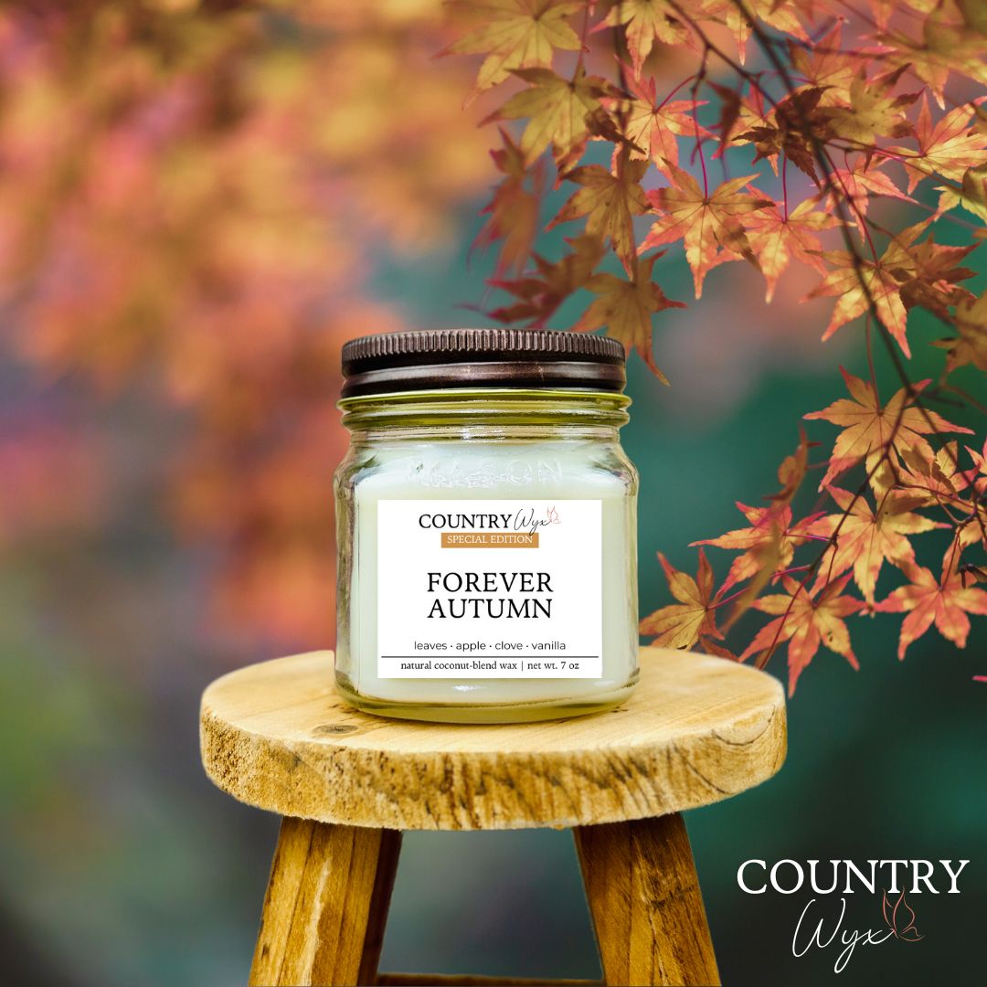 Candle jar labeled &#39;Forever Autumn&#39; on a wooden stool with autumn leaves in the background