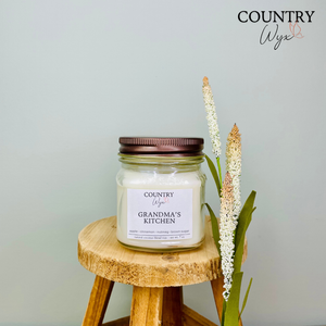 Grandma's Kitchen 8oz candle by Country Wyx displayed on a wooden stool with a soft farmhouse-inspired background