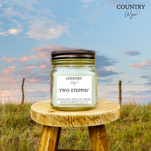 Two Steppin' 8oz candle by Country Wyx on a wooden stool with a Nebraska Sandhills background