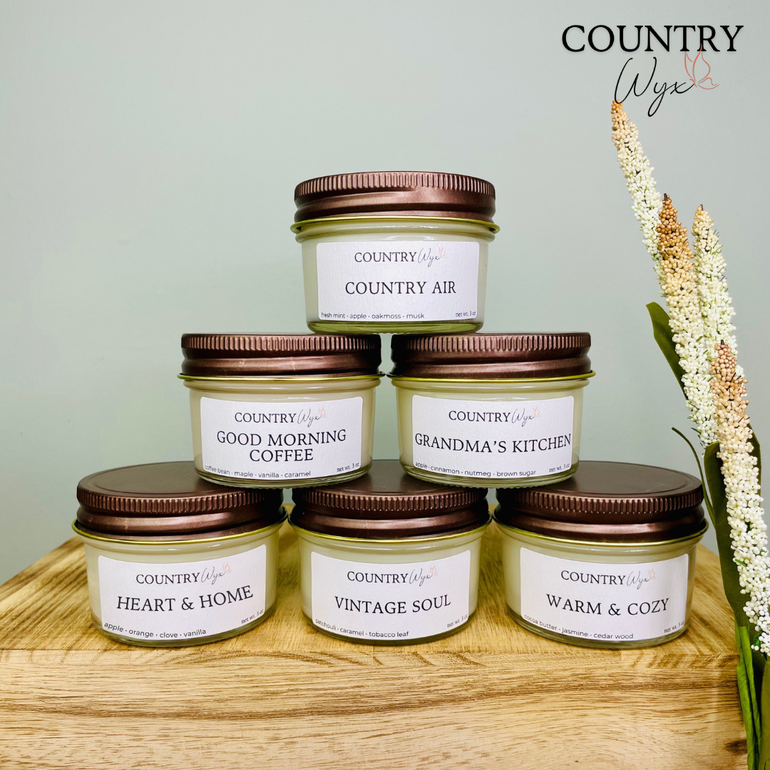 Country Wyx fall sample pack candles stacked on a wooden surface with farmhouse-inspired decor, featuring Country Air, Good Morning Coffee, Grandma’s Kitchen, Heart &amp; Home, Vintage Soul, and Warm &amp; Cozy