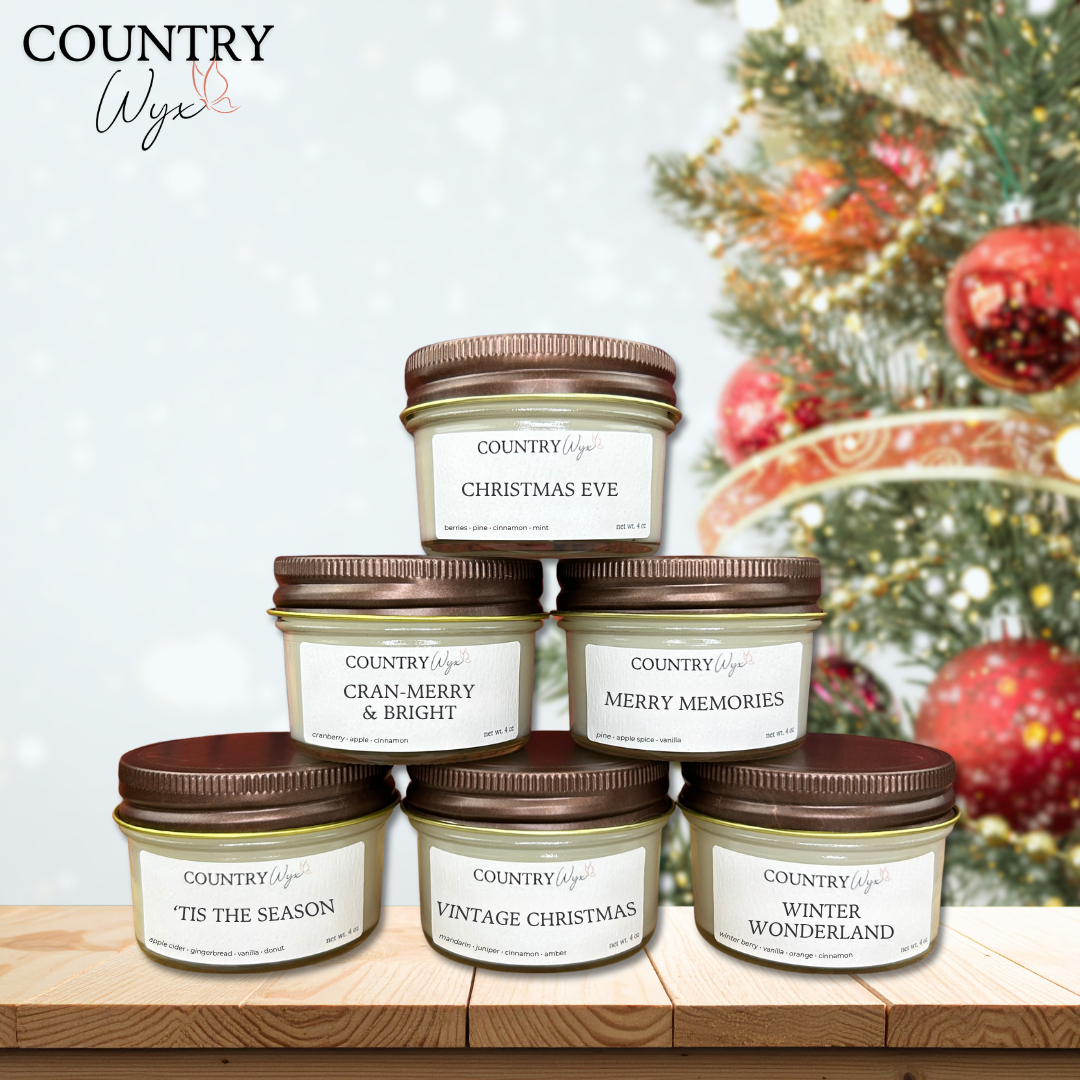 Winter Sample Pack of Country Wyx 4oz candles with holiday-themed labels on a wooden stand against a blurred Christmas tree with ornaments background.