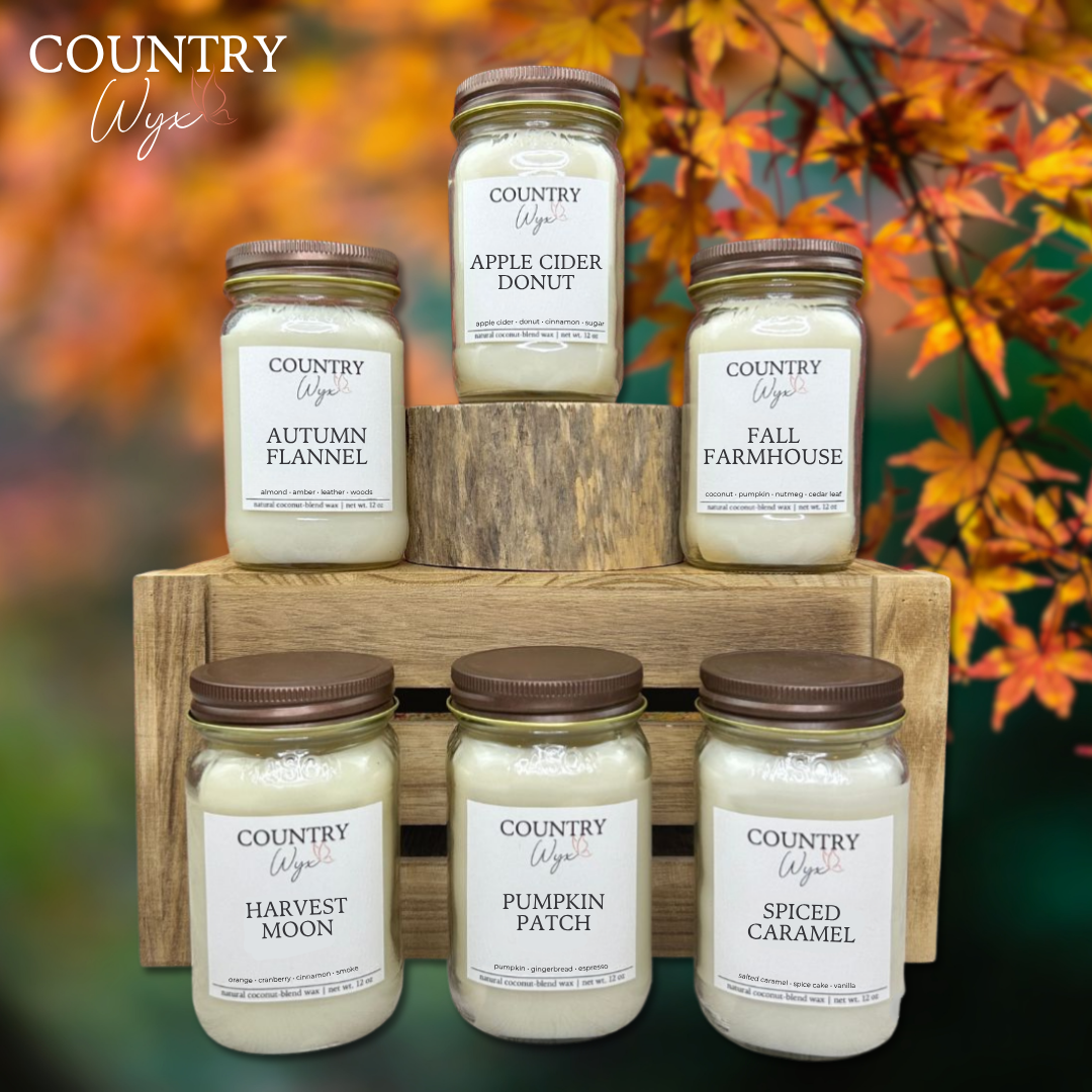 Fall Collection of Country Wyx 16oz candles with autumn-themed labels on a wooden stand against an autumn leaf background.
