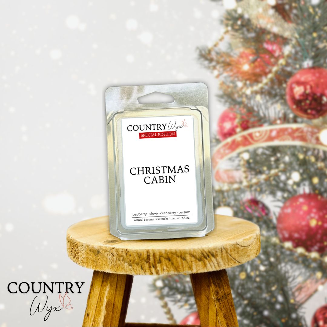 Country Wyx Christmas Cabin wax melt on wooden stool with Christmas tree in background.