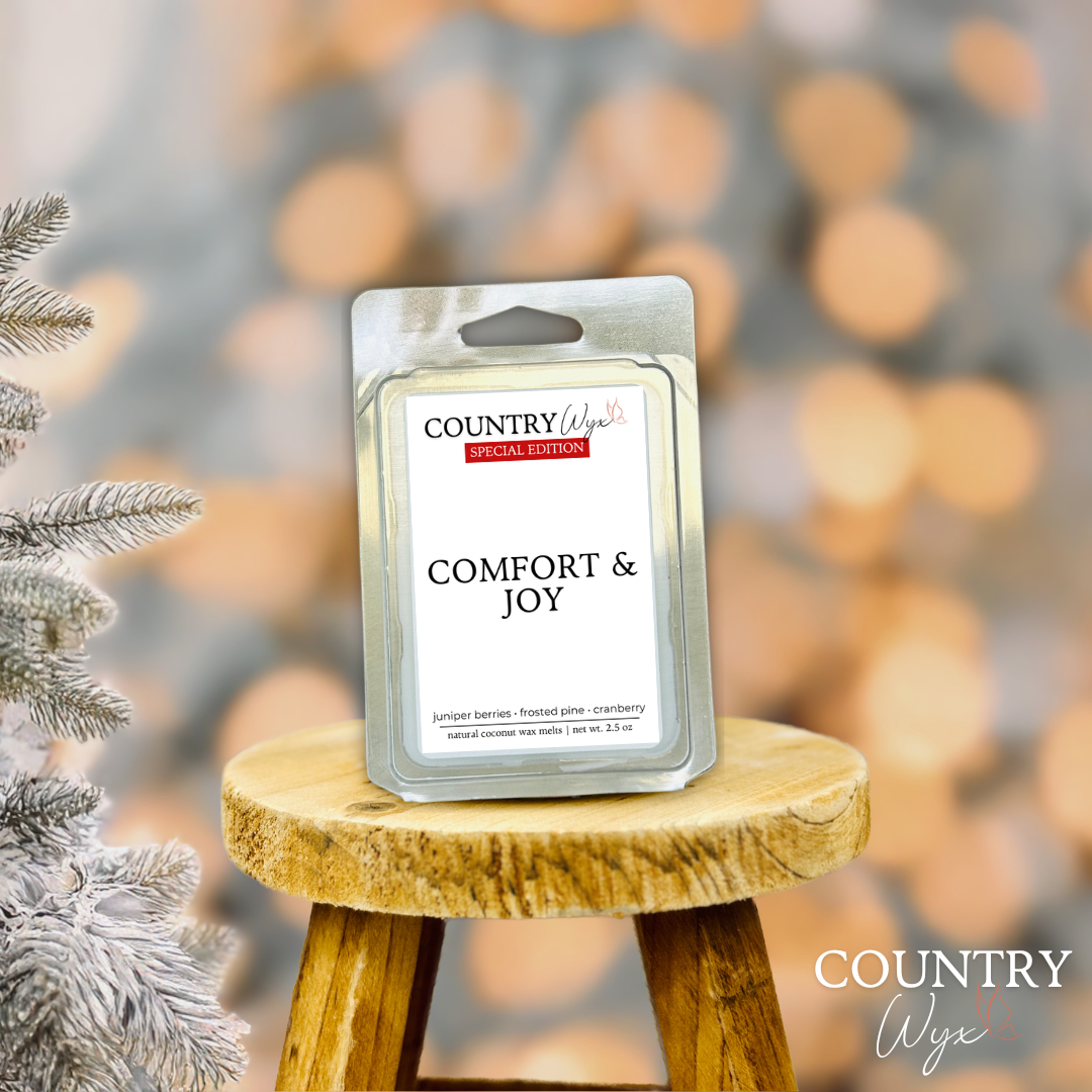 Comfort & Joy wax melt by Country Wyx on a wooden stool with a frosted pine tree holiday background